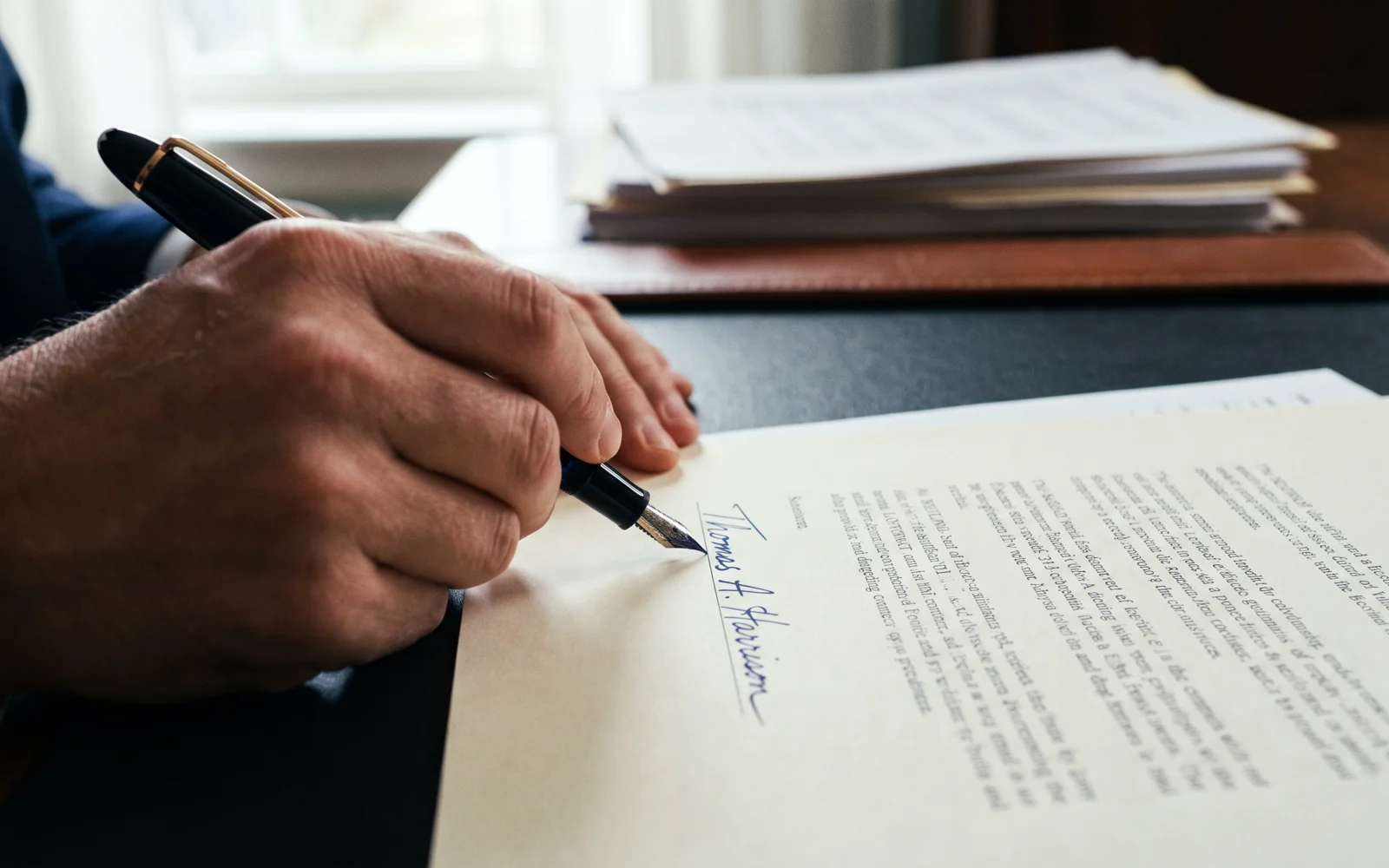 A hand signing a document on a signature line, in a navy duotone.